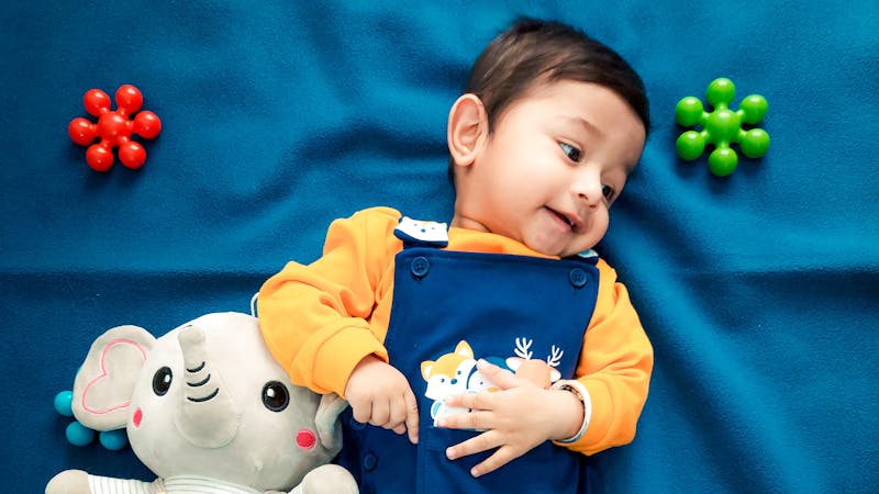 Babyjongen in zachte newborn kleding met blauwe tuinbroek en geel shirt